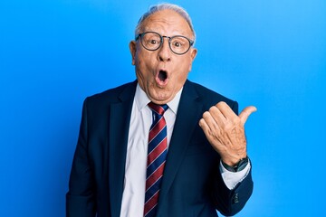 Canvas Print - Senior caucasian man wearing business suit and tie surprised pointing with hand finger to the side, open mouth amazed expression.