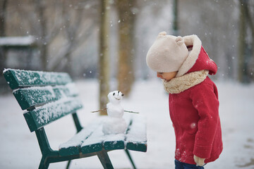 Adorable toddler girl building a snowman on a day with heavy snowfall