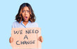© Krakenimages.com - Young beautiful mixed race woman holding we need a change banner scared and amazed with open mouth for surprise, disbelief face