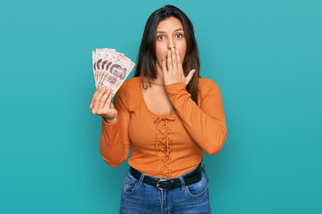 Sticker - Beautiful hispanic woman holding mexican pesos covering mouth with hand, shocked and afraid for mistake. surprised expression