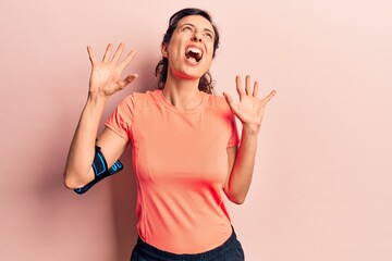 Wall Mural - Young beautiful hispanic woman wearing sportswear using smartphone crazy and mad shouting and yelling with aggressive expression and arms raised. frustration concept.