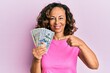 © Krakenimages.com - Middle age hispanic woman holding dollars smiling happy pointing with hand and finger