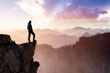 composite. adventurous man hiker with hands up on top of a steep rocky cliff. sunset or sunrise. lan