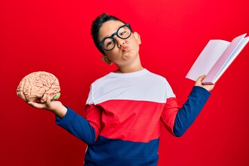 Sticker - Little boy hispanic kid holding brain studying for school looking at the camera blowing a kiss being lovely and sexy. love expression.