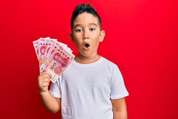 Sticker - Little boy hispanic kid holding yuan chinese banknotes scared and amazed with open mouth for surprise, disbelief face