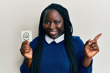 Sticker - Young black woman with braids holding email symbol on paper smiling happy pointing with hand and finger to the side