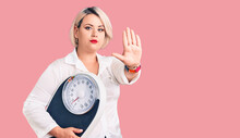 Young Blonde Plus Size Woman Holding Weighing Machine With Open Hand Doing Stop Sign With Serious And Confident Expression, Defense Gesture