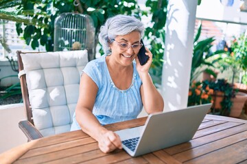 Wall Mural - Middle age woman with grey hair smiling happy relaxing sitting at the terrace working from home