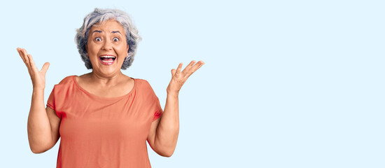 Poster - Senior woman with gray hair wearing orange tshirt celebrating victory with happy smile and winner expression with raised hands