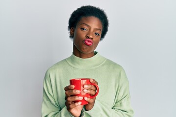 Sticker - Young african american girl drinking a cup of coffee looking at the camera blowing a kiss being lovely and sexy. love expression.