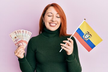 Poster - Beautiful redhead woman holding colombia flag and 10 colombian pesos banknotes sticking tongue out happy with funny expression.