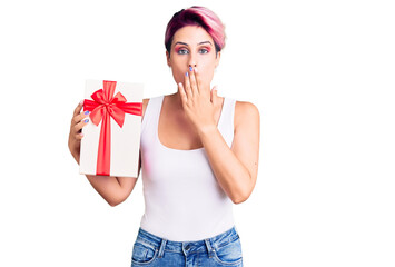 Sticker - Young beautiful woman with pink hair holding gift covering mouth with hand, shocked and afraid for mistake. surprised expression