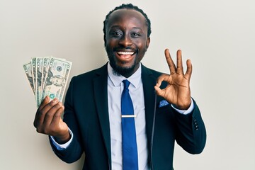 Sticker - Handsome young black man wearing business suit holding 20 dollars banknotes doing ok sign with fingers, smiling friendly gesturing excellent symbol