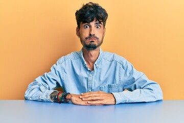 Poster - Young hispanic man wearing casual clothes sitting on the table puffing cheeks with funny face. mouth inflated with air, crazy expression.