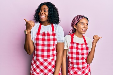 Sticker - Beautiful african american mother and daughter wearing baker uniform pointing thumb up to the side smiling happy with open mouth