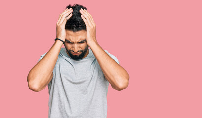 Wall Mural - Young man with beard wearing casual grey tshirt suffering from headache desperate and stressed because pain and migraine. hands on head.