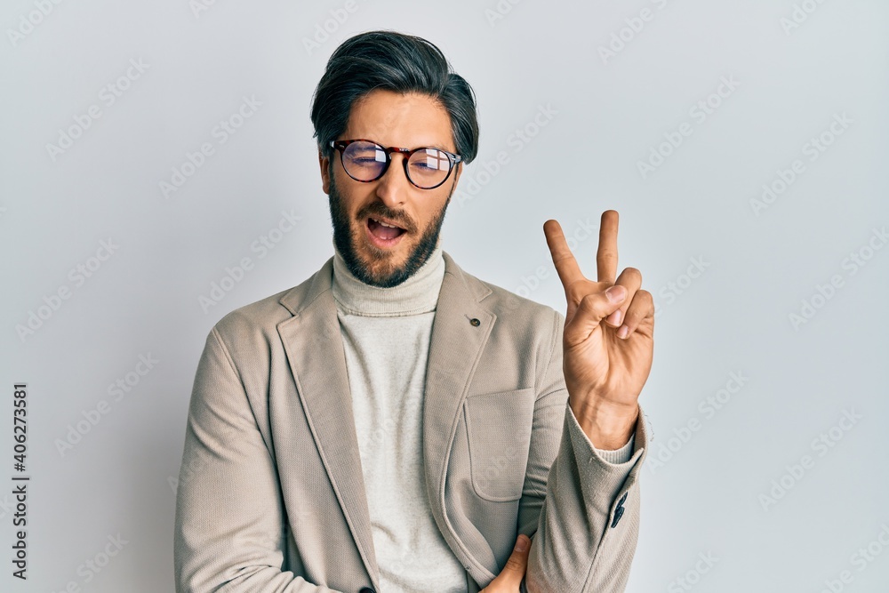 Young hispanic man wearing business jacket and glasses smiling with happy face winking at the camera doing victory sign. number two.