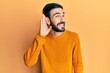 © Krakenimages.com - Young hispanic man wearing casual clothes smiling with hand over ear listening an hearing to rumor or gossip. deafness concept.