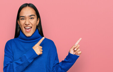 Poster - Young asian woman wearing casual winter sweater smiling and looking at the camera pointing with two hands and fingers to the side.