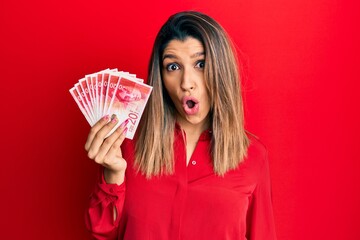 Sticker - Beautiful brunette woman holding 20 israel shekels banknotes scared and amazed with open mouth for surprise, disbelief face