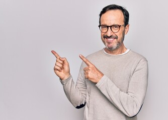 Middle age handsome man wearing casual sweater and glasses over isolated white background smiling and looking at the camera pointing with two hands and fingers to the side.