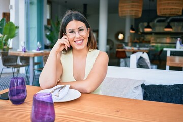 Young beautiful hispanic woman smiling happy. Sitting on the table looking at the camera at restaurant