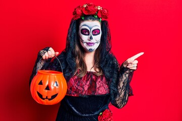 Canvas Print - Young woman wearing day of the dead costume holding pumpkin smiling happy pointing with hand and finger to the side