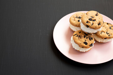 Homemade Chocolate Chip Cookie Ice Cream Sandwich on a pink plate on a black background, side view. Copy space.