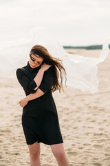 Wall Mural - Woman loneliness. Female abuse. Protection safety. Portrait of hurt insecure brunette lady in black dress with flying away hair in cold wind standing on sandy fall beach.