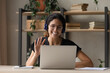 © fizkes - Smiling Caucasian woman in headphones wave greet to camera talking on video call on laptop. Happy young female in glasses and earphones have webcam digital conference or meeting on computer.