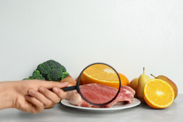 Wall Mural - woman with magnifying glass exploring raw meat and fruits, space for text. poison detection