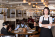 © JackF - Portrait of confident young waitress with arms crossed in cozy busy restaurant
