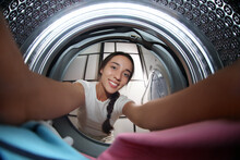 Young Woman Putting Clothes Into Washing Machine In Bathroom, View From Inside