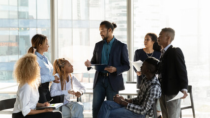 Diverse multiethnic businesspeople gather at casual meeting in office, brainstorm over business project together. Multiracial colleagues talk discuss company financial paperwork. Teamwork concept.