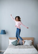 © BestForYou - Happy young woman jumping on the bed at home.