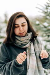 Adult young woman with sparklers on the background of winter pine forest