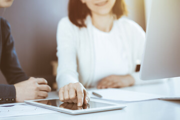 Businesswoman pointing at tablet computer screen while giving presentation to her female colleague. Group of business people working at the desk in office. Teamwork concept