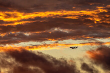 A Commercial Airline Plane Descends Through Clouds At Sunset.
