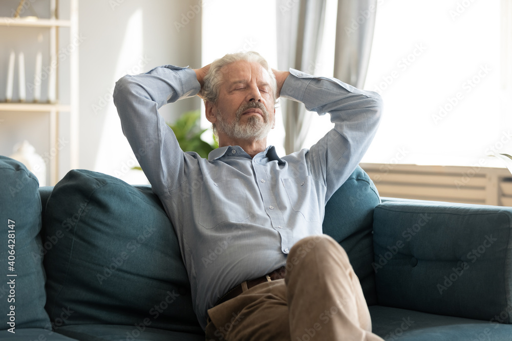 Relaxed smiling middle aged mature grey-haired man resting with closed eyes on cozy couch, enjoying stress free sweet tranquil weekend time alone indoors, daydreaming or meditating alone at home. - obrazy, fototapety, plakaty 