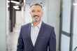 © sofiko14 - Close up front view of happy 50-aged bearded businessman in formal wear, posing to camera with smile, while standing in modern light office corridor. Indoor portrait of mature office worker