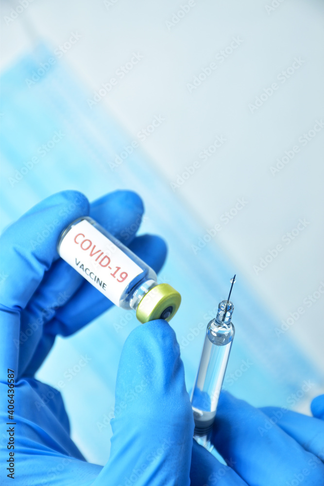 A doctor wearing blue gloves holds a bottle of COVID-19 vaccine.