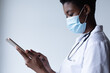© Wavebreak Media - Mixed race female doctor wearing face mask standing and using digital tablet