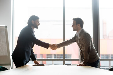 Happy two male business partners shaking hands, starting negotiations meeting or making agreement in boardroom. Confident businessman welcoming client or celebrating signing contract in office.