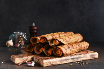 Wall Mural - Pancakes with liver and stuffing with carrots on a wooden board on a dark background.