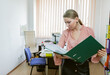 © splitov27 - Office worker woman examines documents in a folder while standing against the background of office workspace