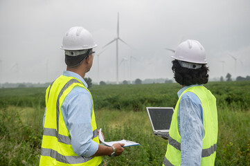 Two engineers working and holding the report at wind turbine farm Power Generator Station on mountain,Thailand people