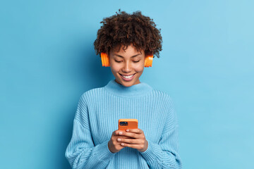 Wall Mural - smiling teenager with afro hair listens favorite music track holds mobile phone downloads song to he