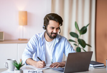 online education. young arab guy watching webinar on laptop and taking notes