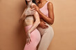 © WHstudio Leushin N - Cropped shot of two women stand closely to each other have different skin conditions wear cropped top and leggings isolated over brown background