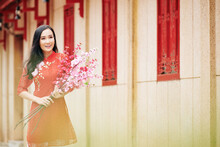 Attractive Smiling Young Asian Woman In Red Dress Standing Outdoors With Blooming Peach Branches